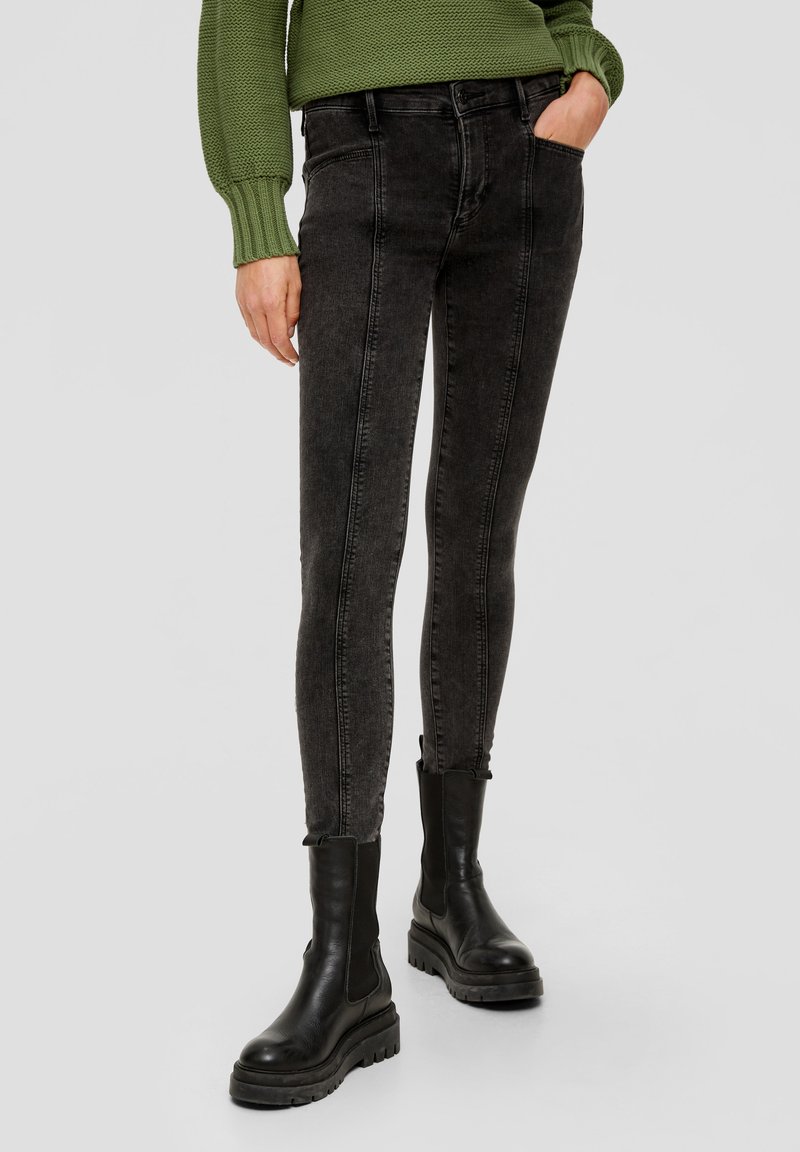 Czarne dżinsy z wysokim stanem i dopasowanym krojem, z pięcioma kieszeniami i delikatnym efektem przetarcia. Połączone z masywnymi, czarnymi botkami za kostkę.