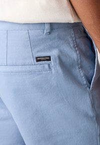 Svijetloplave pamučne hlače s stražnjim džepom i crnom oznakom "SCOTCH & SODA", ravnim prednjim dijelom i glatkom teksturom.