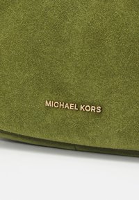 Roheline sametist käekott, millel on sile tekstuur ja esiküljel kuldne "MICHAEL KORS" logo detail. Disain on ristkülikukujuline.