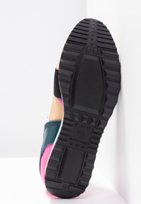 Semelle d'une basket multicolore avec un motif de bande de roulement épais noir, montrant une adhérence texturée et le texte "Made in China" près du talon.