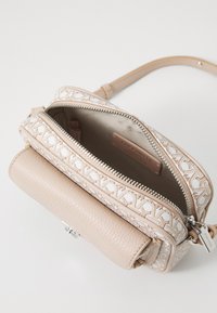 Borsa a tracolla beige in pelle testurizzata, con motivo logo ricamato, chiusura con cerniera e tracolla regolabile. L'interno aperto mostra la fodera.