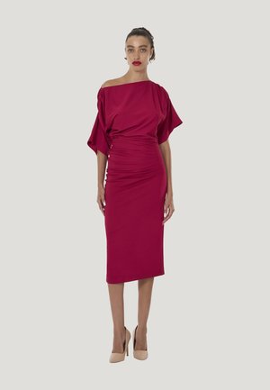 Figurbetontes, schulterfreies Kleid in einem satten Burgunderton, mit weichem, drapiertem Stoff und Raffung, kombiniert mit nudefarbenen High Heels.