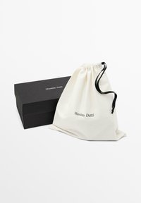 Borsa a sacco in tela beige con dettagli neri, con la scritta "Massimo Dutti" stampata in nero. Include una scatola rettangolare nera.
