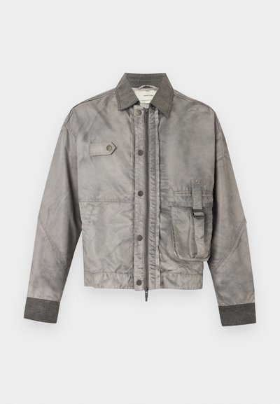 Γκρι μακρυμάνικο μπουφάν με μπροστινό φερμουάρ και κουμπιά, θήκη στο στήθος με καπάκι και πλαϊνή θήκη με λεπτομέρεια αγκράφας.