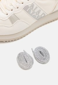Sneaker crema con materiali testurizzati e una fascia argentata con la scritta "NAP". Include due paia di lacci argentati.