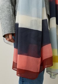 Bufanda ligera con rayas horizontales en azul, crema, azul marino, rojo y amarillo, con un tejido texturizado y un acabado translúcido.