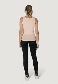 Top aderente rosa con spalline larghe, abbinato a jeans skinny neri. L'outfit presenta una texture liscia e un design minimalista.
