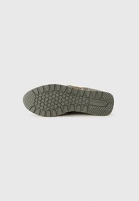 Semelle en caoutchouc verte avec un motif de grip texturé et des points en relief, présentant un design ondulé vers le talon et un logo sur le côté.