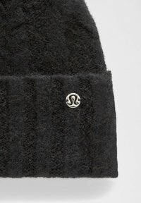 Gorro de punto negro con textura acanalada y un pequeño logo plateado en el dobladillo. Hecho de material suave y peludo.