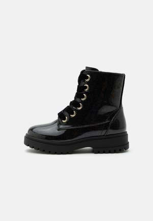 Botte de combat en cuir verni noir avec semelle à crampons épaisse, lacets en ruban de velours et œillets dorés, vue de profil.