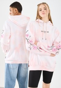 Felpa con cappuccio di un rosa chiaro con motivo tie-dye, caratterizzata da ricami floreali sulle maniche e una grafica testuale frontale. Materiale misto cotone.