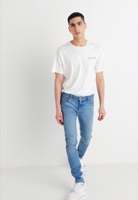 Camiseta blanca de algodón con un logotipo colorido, combinada con jeans de mezclilla azul claro y zapatillas blancas, con un ajuste slim y un diseño sencillo.