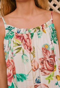 Robe sans manches à motif floral avec un col froncé ; présente des fleurs roses, vertes et bleues sur un fond crème clair. Texture de tissu douce.