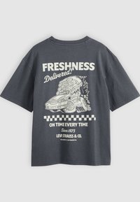 T-shirt gris foncé avec un graphisme blanc représentant une voiture rapide transportant une part de pizza et le texte : « Fraîcheur livrée ! Toujours à l'heure. »