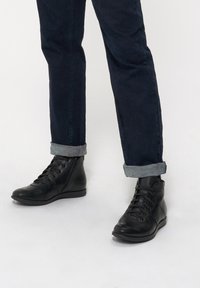 Czarne skórzane botki za kostkę z zaokrąglonym czubkiem, sznurowanym przodem, bocznym zamkiem błyskawicznym i niskim koturnem, zestawione z podwiniętymi ciemnymi dżinsami.
