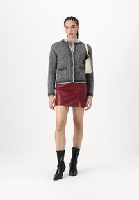 Pelēka teksturēta jaka ar krēmkrāsas apdari, divas kabatas, apvienota ar sarkanu mākslīgās ādas mini svārku ar sānu šķēlumu un melniem augstiem zābakiem.