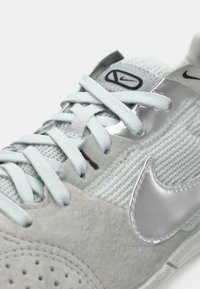 Sneaker grigia e blu chiaro realizzata in materiali scamosciati e in rete, con accenti argentati e lacci piatti, che presenta un logo swoosh sul lato.