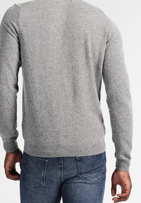 Maglione grigio in lana con una texture liscia, scollo rotondo e maniche lunghe, abbinato a jeans in denim blu con cuciture sulle tasche posteriori.