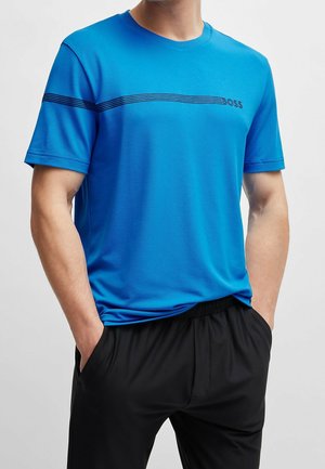 Man wearing a bright blue short-sleeve T-shirt with black horizontal lines and "BOSS" logo, paired with black pants, hands in pockets.