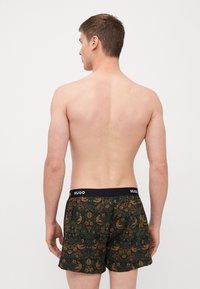 Herren-Boxershorts in Dunkelgrün mit floralem und Vogel-Muster. Schwarzer Bund mit "HUGO"-Logo. Weicher Stoff, lockere Passform.