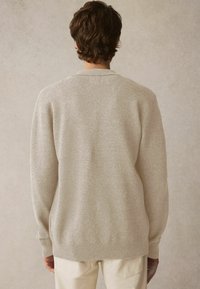 Hellbeiger Pullover mit weicher Textur, gerippten Bündchen und rundem Halsausschnitt. Der Rücken hat einen leicht verlängerten Saum.