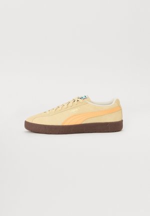 Puma teniske z bež nobučnim zgornjim delom, oranžnim trakom in rjavim gumijastim podplatom. Minimalistična zasnova, oblazinjen ovratnik in klasično vezanje.