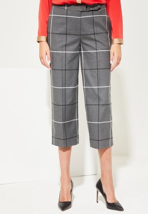 Szare spodnie o kroju cropped z białą i czarną kratą typu windowpane, zestawione z czarnymi szpilkami z zaostrzonym noskiem oraz czerwoną bluzką z złotymi mankietami.