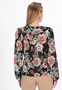 Blusa nera trasparente con ampio motivo floreale rosa e verde. Presenta maniche lunghe e una vestibilità rilassata, con dettagli arricciati sulle spalle.