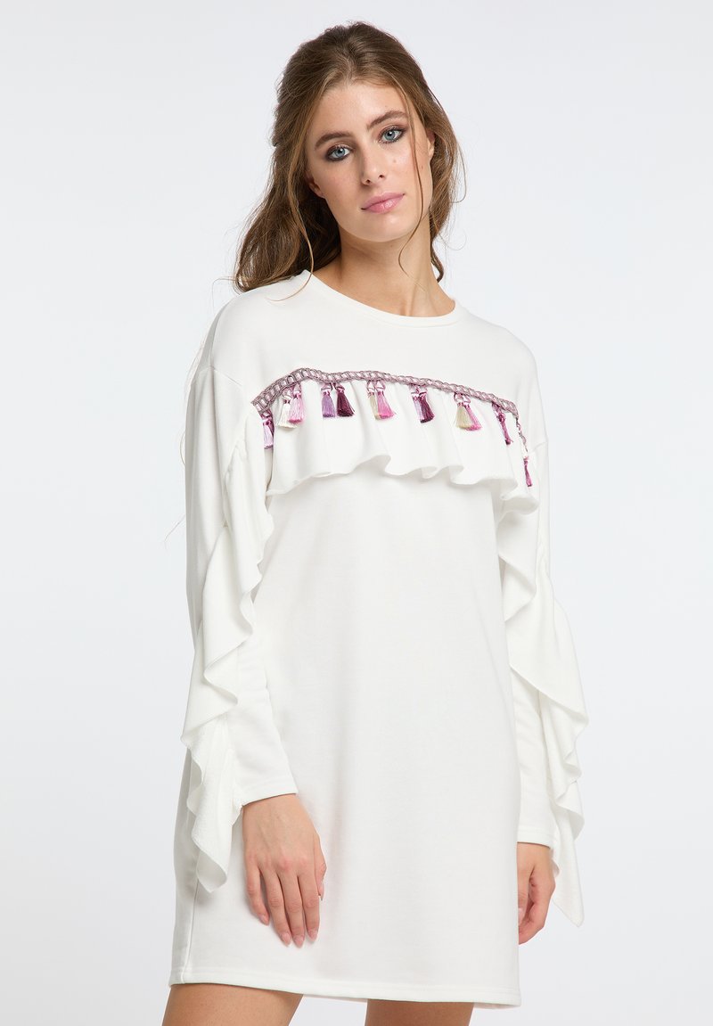 Weißes Kleid mit Rüschensäumen und einem dekorativen Band, das pinke und lila Quasten entlang der Brust ziert. Glatte Textur, lässiges Design.