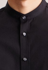 Camicia nera con bottoni a pressione e collo alla coreana, caratterizzata da cinque bottoni piatti, texture liscia e vestibilità su misura.