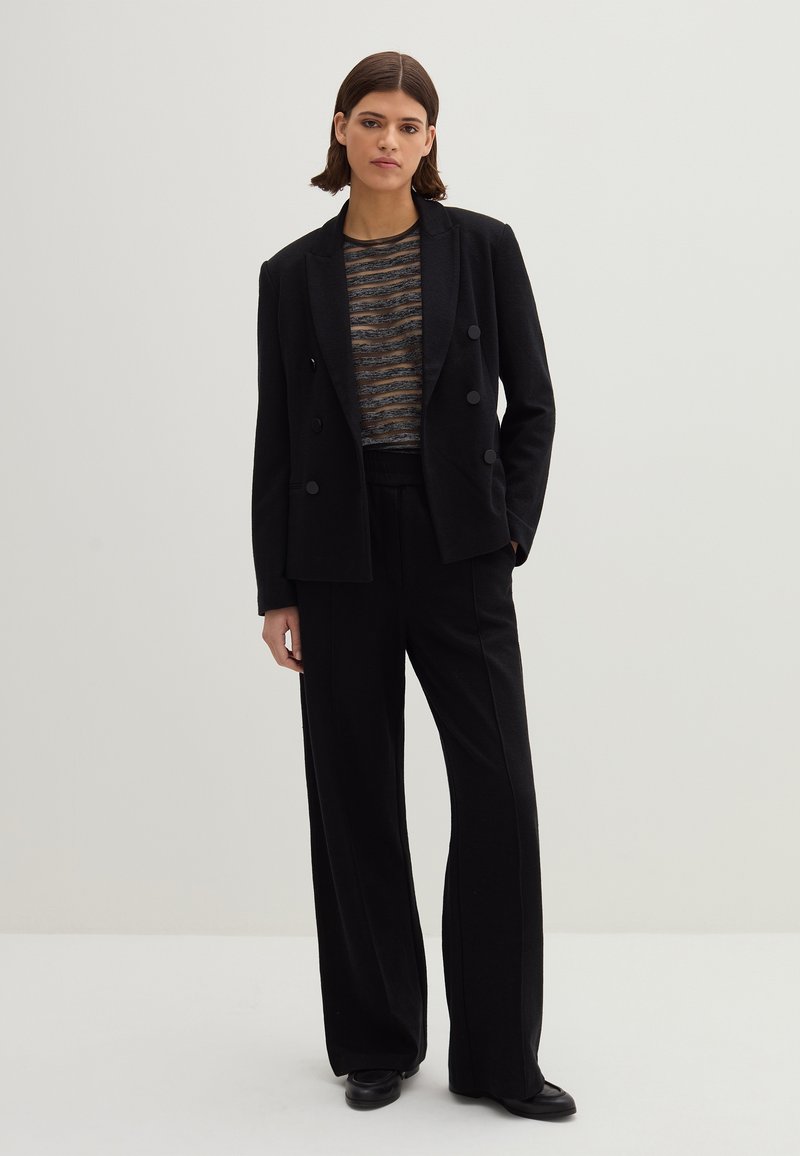 Schwarzes doppelt-knöpfbares Blazer mit großen Knöpfen, kombiniert mit einem strukturierten gestreiften Oberteil und weit geschnittenen Hosen. Glatter Stoff mit taillierter Silhouette.