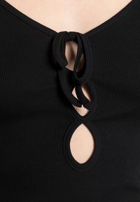 Bodysuit preto com nervuras apresentando um design em forma de buraco-chave com um detalhe em nó na gola. Textura suave com uma silhueta ajustada.