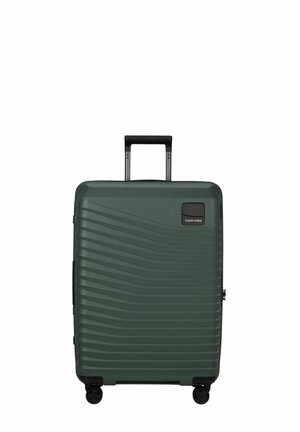 Valise rigide vert foncé à rainures horizontales, poignée télescopique noire déployée, et quatre roues pivotantes noires.