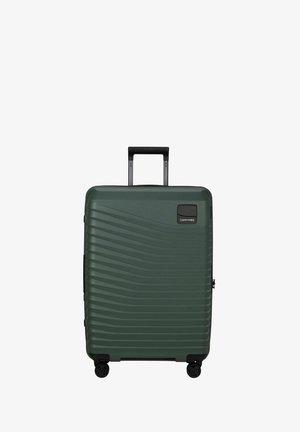 Valise rigide vert foncé à rainures horizontales, poignée télescopique noire déployée, et quatre roues pivotantes noires.