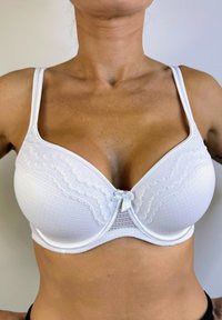 Sostén blanco con tela suave, soporte de varilla, copas texturizadas y un pequeño lazo decorativo en el centro. Tiras ajustables.