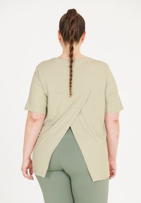 Lys grøn kortærmet top med et buet bagdesign, der har en crossover-detalje. Blødt stof med en ribbet tekstur. Sammen med grønne leggings.