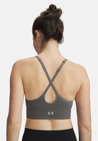 Γκρι αθλητικό σουτιέν με λουριά που διασταυρώνονται στην πλάτη, ριμπ υφή και κυκλικό άνοιγμα. Διαθέτει λογότυπο στην πλάτη και ρυθμιζόμενη μηχανική εφαρμογή.