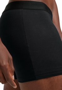 Black cotton boxer shorts with a snug fit, featuring a smooth waistband and subtle stitching details on the sides. Soft texture.