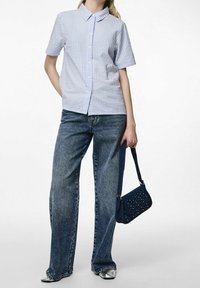 Camicia a righe a maniche corte in azzurro chiaro e bianco, abbinata a jeans blu a vita alta. Una borsa a tracolla perforata blu navy completa il look.