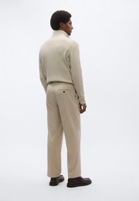 Beige ribbestrikket genser med høy hals og lyse beige bukser med rett passform, kombinert med mørkebrune sko. Minimalistisk design med subtile detaljer.