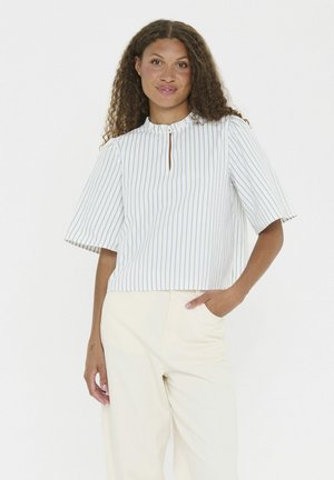 Blusa bianca a righe verticali verdi, maniche corte, scollatura a chiave e vestibilità rilassata, abbinata a pantaloni chiari.