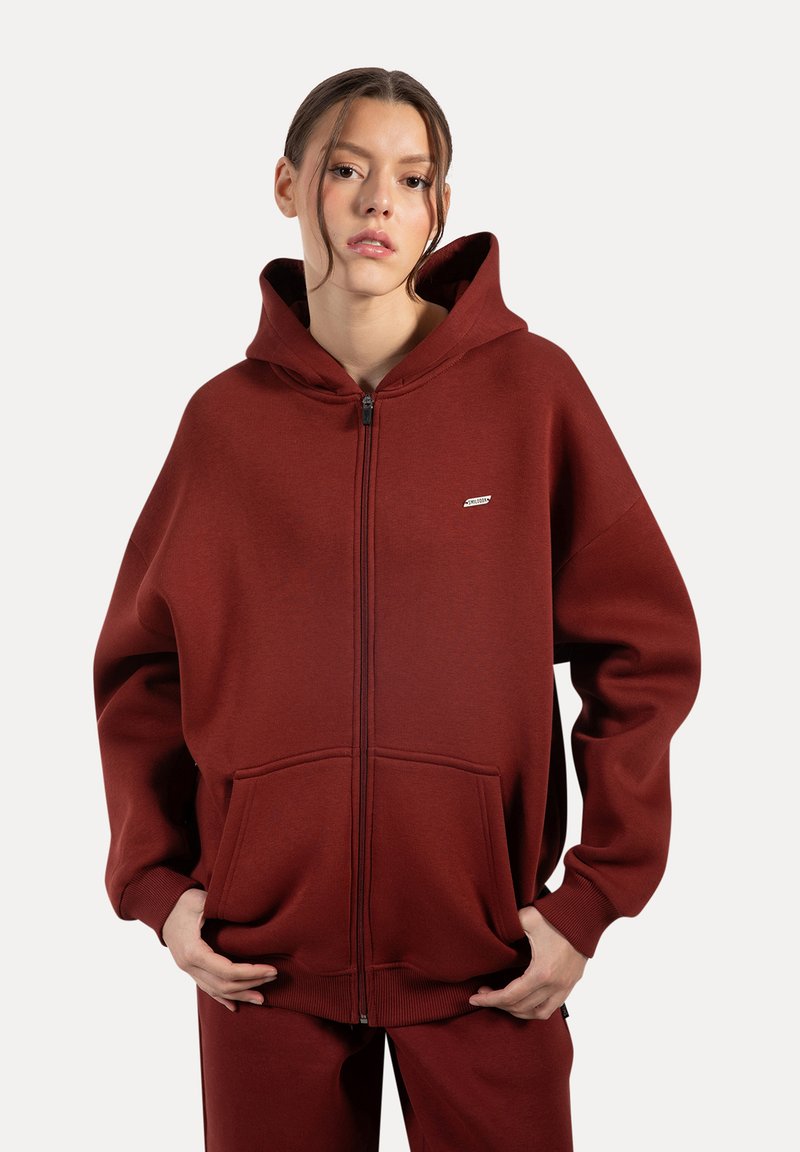 Bordeaux zip-up hoodie gemaakt van zachte stof met een grote voorzak en geribde manchetten. Bevat een capuchon en een klein logo-detail.
