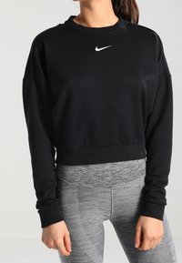 Czarny krótki sweatshirt z długimi rękawami, z teksturowanym wykończeniem i białym logo Nike na klatce piersiowej, w połączeniu z szarymi legginsami w wzory.
