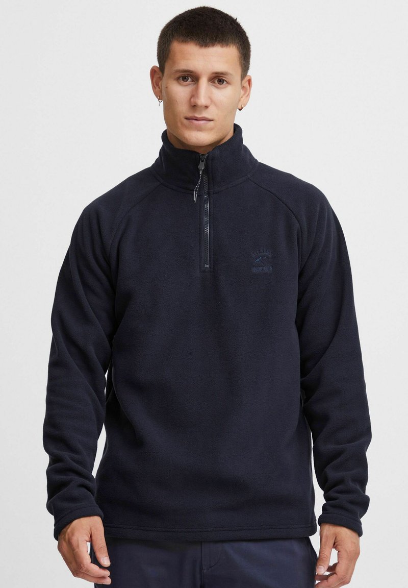 Marinblå fleecepullover med hög krage, halv dragkedja och långa ärmar. Har en liten logotyp på bröstet och en mjuk, texturerad yta.