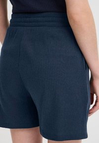 Close-up of a person wearing navy blue ribbed knit shorts with a pocket, cropped from waist to mid-thigh.
