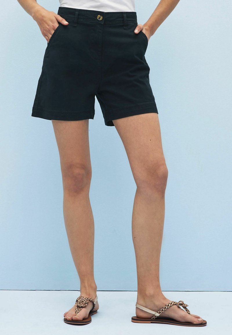 Černé bavlněné šortky se střihovým rovný střih, s knoflíkovým zapínáním, bočními kapsami a čistým lemem. V kombinaci s hnědými plochými sandály.