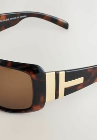 Bruņu bruņurupuču krāsas saulesbrilles ar brūnām stikliņām, melnu rāmīti, zelta akcentiem sānos un taisnstūra formu.