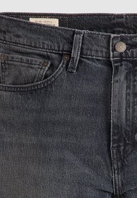 Jean en denim noir en gros plan montrant une poche avant, une boucle de ceinture et une fermeture par bouton avec étiquette en tissu visible à l'intérieur.