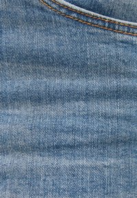 Denimtyg i mellanblått med twill-väv, som har orange sömmar längs kanterna och en mjuk, något texturerad yta.