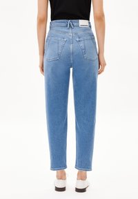 Vaqueros de mezclilla de cintura alta en azul claro con diseño de pierna recta, bolsillos traseros visibles y una etiqueta blanca en la cintura. Textura suave.